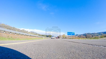 Photo for On a crisp winter day, a car cruises along the iconic Highway 1 near San Luis Obispo, California. The surrounding landscape is brownish and subdued, with rolling hills and patches of coastal - Royalty Free Image