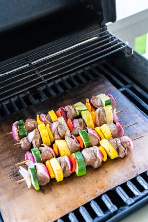 Foto de Skewered carne de res y verduras frescas chisporrotean en una estera de cobre parrilla sobre una parrilla de gas al aire libre. - Imagen libre de derechos