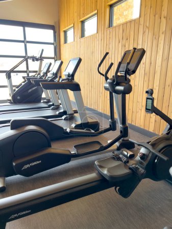 Photo for Denver, Colorado, USA-March 3, 2024-The spacious gym is outfitted with a variety of modern exercise machines, bathed in natural light from large windows, set against a warm wooden ceiling backdrop. - Royalty Free Image