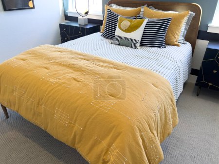 Photo for This cheerful bedroom combines crisp striped bedding with eye-catching mustard yellow throws and pillows, balanced by a navy bedside table and lamp. The space is anchored by a classic wood headboard - Royalty Free Image