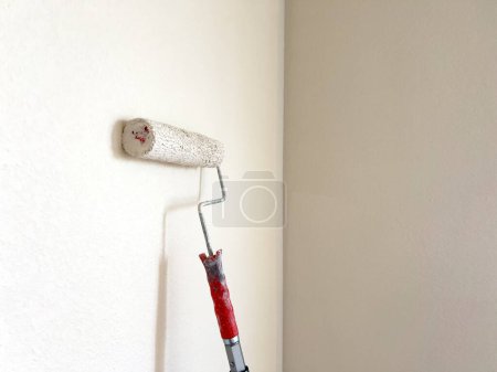 Photo for Detailed process of painting a wall, with a focus on a paint roller applying a fresh white coat, symbolizing the transformative power of a simple home improvement task. - Royalty Free Image