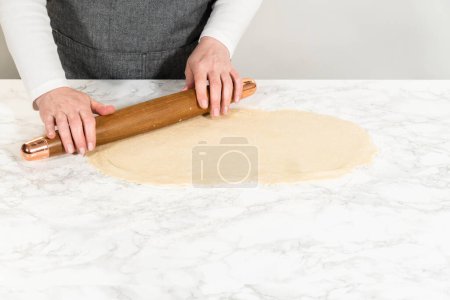 Téléchargez les photos : Rouler la pâte à pain avec un rouleau à pâtisserie français pour cuire des petits gâteaux à la cannelle sans levure. - en image libre de droit
