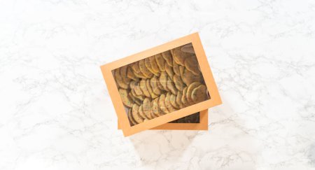 Téléchargez les photos : Pose plate. Les biscuits au sucre, remplis de saupoudres mélangées dans la pâte, sont soigneusement disposés avec une précision méticuleuse dans une boîte en papier brun rustique. - en image libre de droit