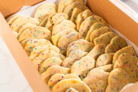 Photo for The sugar cookies, filled with sprinkles mixed into the dough, are carefully arranged with meticulous precision into a rustic brown paper box. - Royalty Free Image