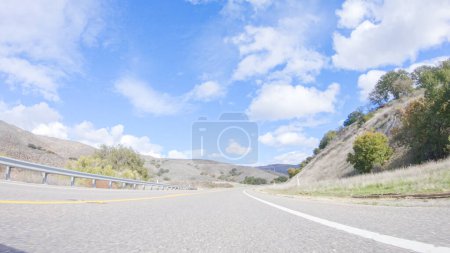 Vehicle is cruising along the Cuyama Highway under the bright sun. The surrounding landscape is illuminated by the radiant sunshine, creating a picturesque and inviting scene as the car travels