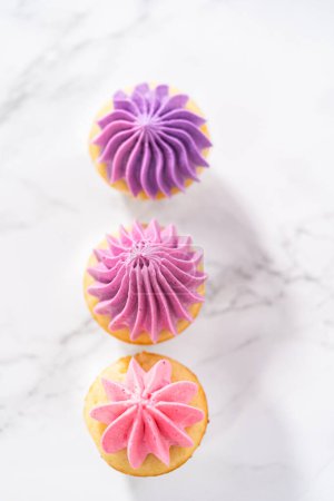 Foto de Mini cupcakes de vainilla recién horneados con glaseado de crema de mantequilla rosa ombre en un ocunter de cocina de mármol. - Imagen libre de derechos