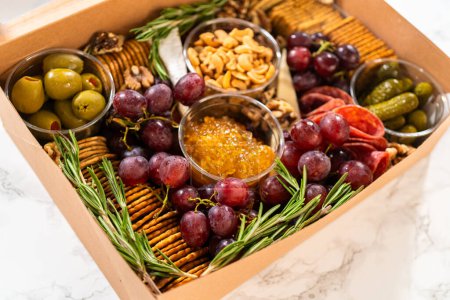 Photo for Charcuterie box featuring sliced meat, cheese, crackers, and grapes, all neatly packaged in a brown gifting box. - Royalty Free Image