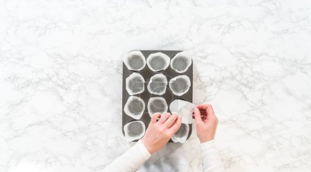 Flat lay. Lining baking cupcake pan with paper tulip liners to bake no-yeast cinnamon roll cupcakes.