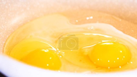 Foto de Las yemas vibrantes brillan, espátula roja en medio de huevos de cocina en una sartén moteada. - Imagen libre de derechos