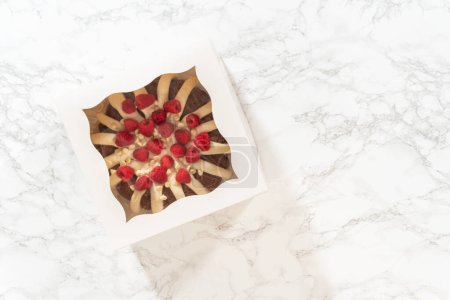 Foto de Acostado. Con cuidado, el pastel de chocolate blanco de Raspberry Bundt se envasa en una caja de papel blanco, lista para regalar para brindar alegría e indulgencia a alguien especial. - Imagen libre de derechos