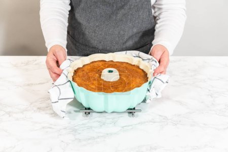 With precision, the bundt cake is carefully removed from the pan - placed onto a round cooling rack, preparing it for a flawless presentation and delightful indulgence.