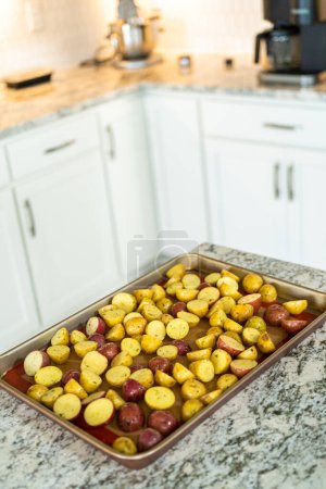 Téléchargez les photos : Dans une cuisine moderne, une gamme de pommes de terre en marbre multicolores et coupées en deux sont disposées sur une plaque de cuisson doublée d'une doublure en silicone. Le processus de torréfaction infuse la cuisine avec un arôme appétissant - en image libre de droit