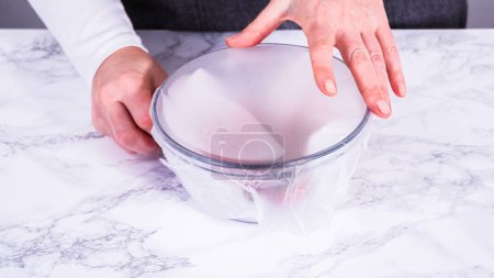 Téléchargez les photos : Les fraises, fraîchement lavées et séchées, sont soigneusement stockées dans un bol en verre doublé d'une serviette en papier et recouvertes d'une pellicule plastique pour maintenir leur fraîcheur.. - en image libre de droit