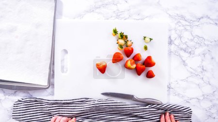 Photo for Flat lay. Succulent red strawberries, some showing early spoilage, are arrayed on a white cutting board, held securely in place, with a paper towel lined glass bowl nearby suggesting an attempt at - Royalty Free Image