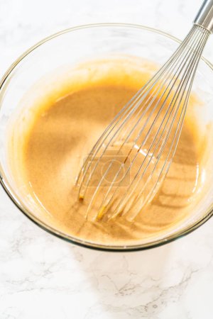 Foto de En un tazón de vidrio grande, los ingredientes se mezclan expertamente para crear la masa para hornear el delicioso pastel de zanahoria Bundt. - Imagen libre de derechos
