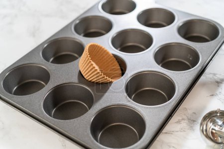 Photo for Getting ready to bake delicious chocolate cupcakes, we carefully line the cupcake pan with paper liners, ensuring a delightful treat awaits. - Royalty Free Image