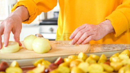 In the welcoming setting of a modern kitchen, a young man continues his dinner preparation process. Hes currently involved in slicing yellow onions into rings, prepping them for grilling on an