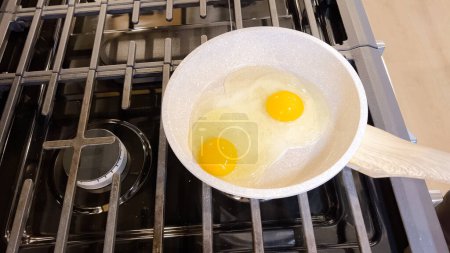 Téléchargez les photos : Dans une poêle antiadhésive, deux œufs parfaitement frits et ensoleillés, prêts à être servis avec une spatule en silicone rouge, sont placés sur une cuisinière.. - en image libre de droit