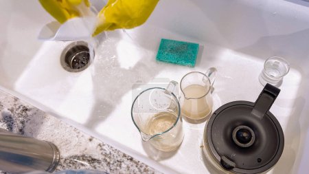 Photo for Yellow-gloved hands are seen washing dishes, scrubbing diligently in a basin sink, surrounded by suds, cleaning utensils, and clear water glasses. - Royalty Free Image