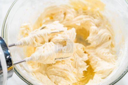 Foto de Combine hábilmente los ingredientes con un mezclador de manos para preparar un glaseado rico y suave de crema de mantequilla de queso, que es perfecto para adornar el pastel de paquete.. - Imagen libre de derechos