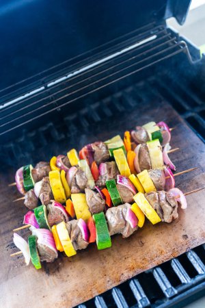 Foto de Skewered carne de res y verduras frescas chisporrotean en una estera de cobre parrilla sobre una parrilla de gas al aire libre. - Imagen libre de derechos