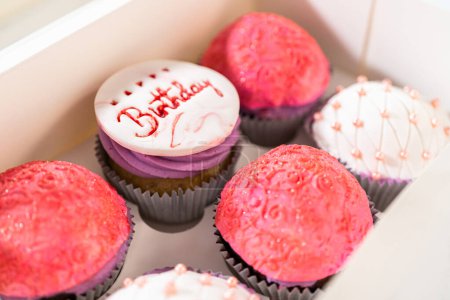 Foto de Los cupcakes de cumpleaños, bellamente adornados con decoraciones fondantes, se colocan cuidadosamente en cajas de papel blanco, listas para su gran presentación. - Imagen libre de derechos