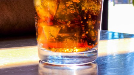 A close-up shot showcases a refreshing glass filled with ice cubes and soda pop, placed on a restaurant table, inviting the viewer to enjoy a cool and fizzy beverage.