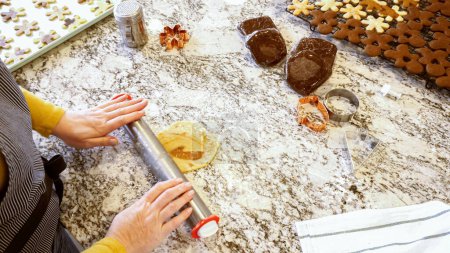 Foto de Usando un rodillo ajustable para desplegar la masa de galletas de jengibre en el elegante mostrador de mármol en una cocina moderna, preparándose para la cocción festiva de las vacaciones.. - Imagen libre de derechos