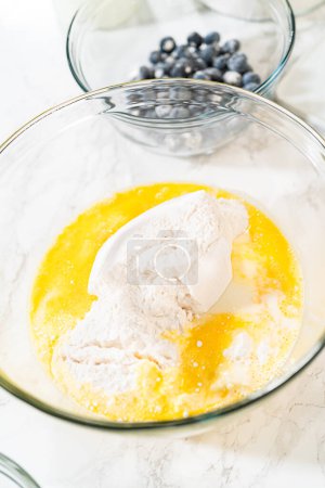 Foto de Integrar los ingredientes en un tazón de vidrio, revolviendo hábilmente con un batidor para elaborar un tentador pastel de limonero y arándano. - Imagen libre de derechos