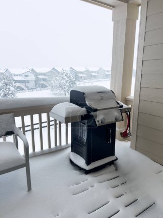 La calma del invierno envuelve una parrilla en una colcha nevada silenciosa, ofreciendo una imagen de serenidad en un balcón suburbano mientras el vecindario yace silenciado bajo una manta invernal blanca.