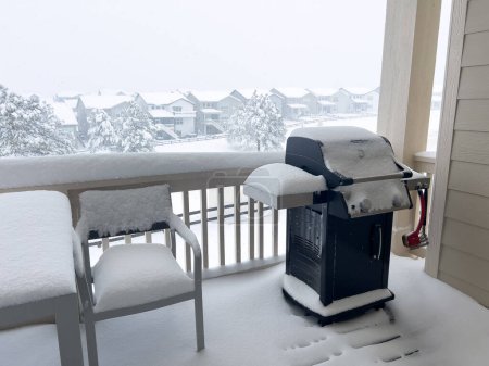 Die Stille des Winters hüllt einen Grill in eine stille Schneedecke und bietet ein Bild der Gelassenheit auf einem Vorstadtbalkon, während die Nachbarschaft unter einer weißen winterlichen Decke liegt..
