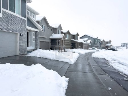 Téléchargez les photos : Neige recouvre une rue de banlieue, où les maisons se tiennent dans le repos calme et les allées révèlent les matins de travail contre les dérives incessantes de l'hiver. - en image libre de droit