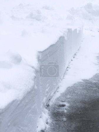 A cleanly shoveled walkway cuts through a thick blanket of snow, revealing a stark contrast against a pristine white barrier.