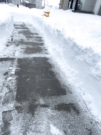 Ein frisch geschaufelter Gehweg schneidet sich durch eine dicke Schneedecke und bietet Durchfahrt in einem vom Winter verwandelten Viertel, während die Häuser Wachposten in der gedämpften Ruhe stehen.