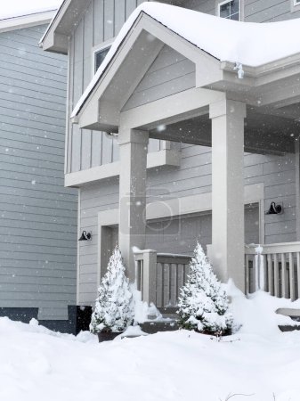 Foto de Los suaves copos de nieve descienden en una acogedora entrada a casa, adornando los abetos y cubriendo el porche con una suave capa invernal. - Imagen libre de derechos