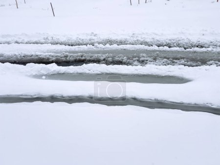 Foto de Las huellas de neumáticos frescos se curvan a lo largo de una calle cubierta de nieve, tallando un camino a través de los copos recién caídos apilados a ambos lados.. - Imagen libre de derechos
