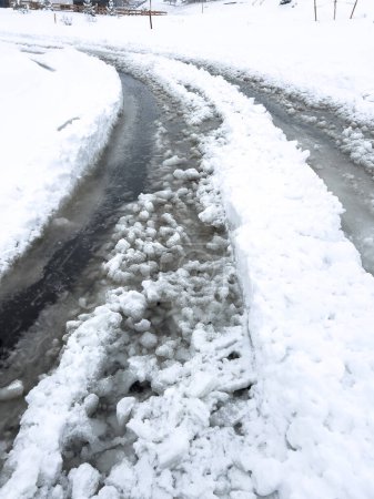 Frische Reifenspuren kurven entlang einer schneebedeckten Straße und bahnen sich einen Weg durch die zu beiden Seiten hoch aufgetürmten frisch gefallenen Flocken.