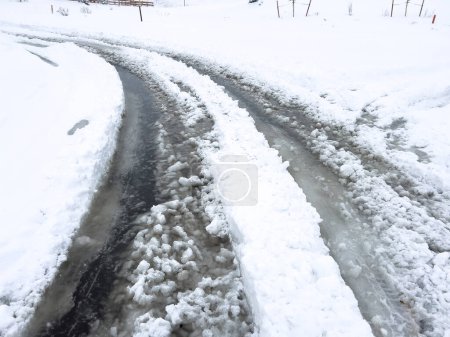 Frische Reifenspuren kurven entlang einer schneebedeckten Straße und bahnen sich einen Weg durch die zu beiden Seiten hoch aufgetürmten frisch gefallenen Flocken.