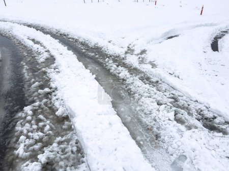 Photo for Fresh tire tracks curve along a snow-covered street, carving a path through the freshly fallen flakes piled high on either side. - Royalty Free Image