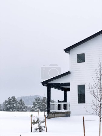 Foto de El marcado contraste de una casa moderna vestida de blanco contra un silencioso telón de fondo nevado evoca una sensación de comodidad aislada en el frío del invierno. - Imagen libre de derechos