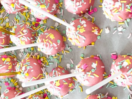 Téléchargez les photos : Arborant soigneusement sur le parchemin, ces gâteaux roses trempés à la main sont un régal ludique, orné d'un arc-en-ciel de saupoudrer qui ajoutent une touche festive aux douces délices. - en image libre de droit