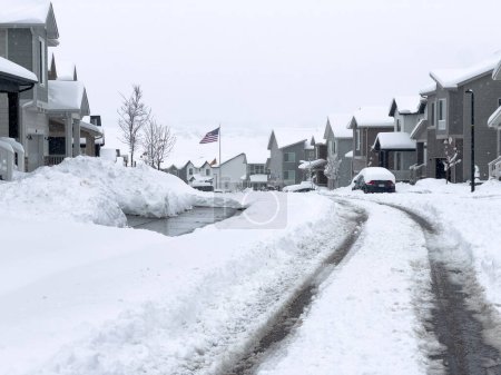 Foto de Castle Rock, Colorado, Estados Unidos-16 de marzo de 2024-Curva de huellas de neumáticos frescos a lo largo de una calle cubierta de nieve, tallando un camino a través de los copos recién caídos apilados a ambos lados. - Imagen libre de derechos