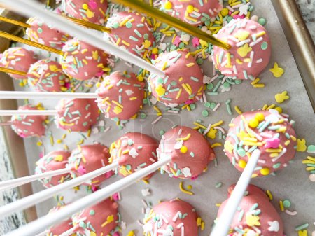 Photo for Arrayed neatly on parchment, these hand-dipped pink cake pops are a playful treat, adorned with a rainbow of sprinkles that add a festive touch to the sweet delights. - Royalty Free Image