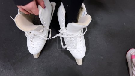 Foto de Castle Rock, Colorado, Estados Unidos-21 de marzo de 2024-En un sincero momento entre bastidores, una joven patinadora artística cuidadosamente ata sus prístinos patines de hielo blanco en preparación para la práctica. - Imagen libre de derechos