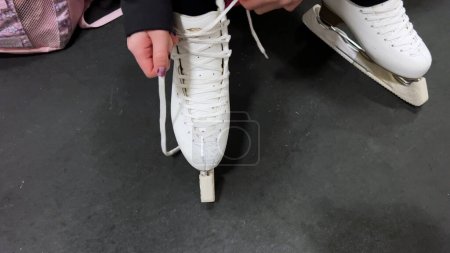 Photo for Castle Rock, Colorado, USA-March 21, 2024-In a candid behind-the-scenes moment, a young figure skater carefully laces up her pristine white ice skates in preparation for practice. - Royalty Free Image