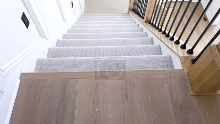 Das Bild fängt das Detail einer gut gestalteten, modernen Treppe ein, die mit einem plüschigen beigen Teppich ausgelegt ist, der durch weiße Wände und Holzgeländer ergänzt wird..