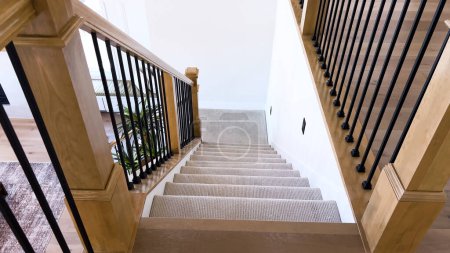 The image captures the detail of a well-designed modern staircase, lined with plush beige carpet, complemented by white walls and wooden balusters.