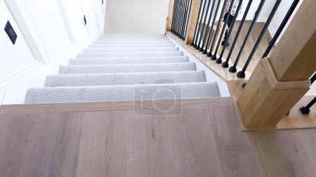 L'image capture le détail d'un escalier moderne bien conçu, doublé d'un tapis beige moelleux, complété par des murs blancs et des balustres en bois.