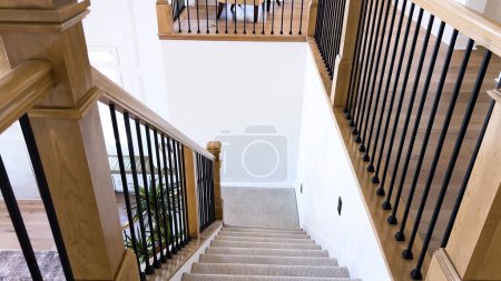 Das Bild fängt das Detail einer gut gestalteten, modernen Treppe ein, die mit einem plüschigen beigen Teppich ausgelegt ist, der durch weiße Wände und Holzgeländer ergänzt wird..