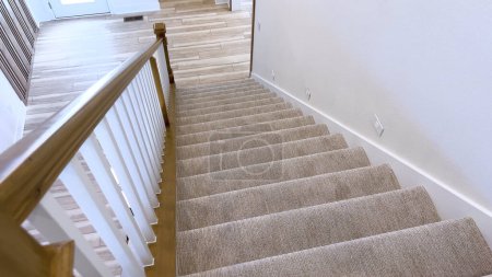 The image captures the detail of a well-designed modern staircase, lined with plush beige carpet, complemented by white walls and wooden balusters.